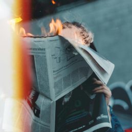 Oseba drži časopis pred obrazom, medtem ko zgornji del časopisa gori. Plameni požirajo robove strani, kar ustvarja vizualno močno podobo uničenja informacij ali krhkosti novic. Fotografija ima dramatičen ton in simbolizira hitro spreminjajoče se diskurze v kriznih obdobjih.